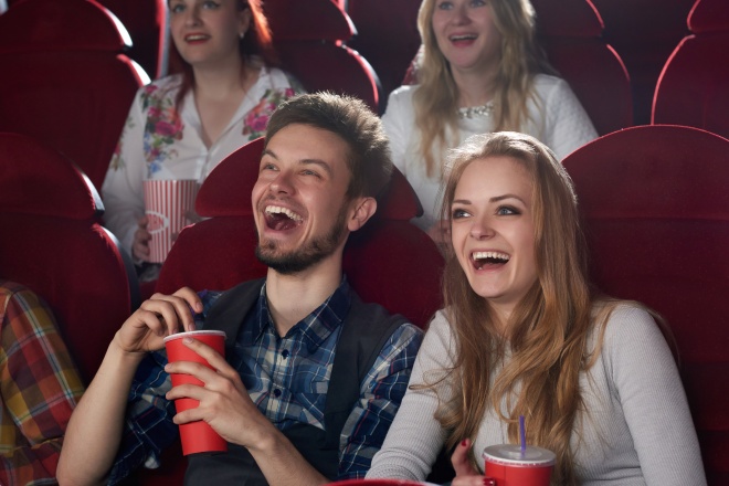 Boyfriend and girlfriend surprised smiling watching comedy movie at cinema.